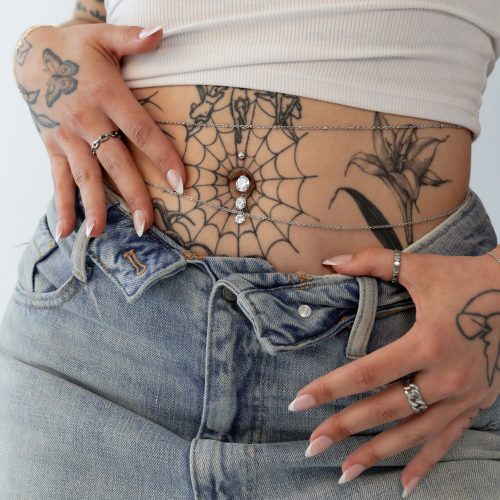 Drei-strängiges Bananabell mit Kristallen an einem tätowierten Bauch mit Jeans.