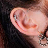 Nahaufnahme eines Ohrs mit mehreren funkelnden Piercings, darunter ein Triple Labret Pushfit, auf hellem Hintergrund