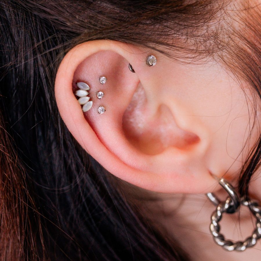 Nahaufnahme eines Ohrs mit mehreren funkelnden Piercings, darunter ein Triple Labret Pushfit, auf hellem Hintergrund