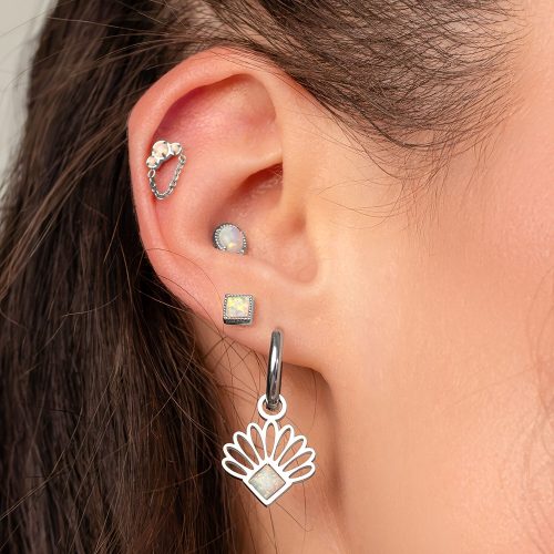 Nahaufnahme eines Ohrs mit mehreren Piercings, darunter ein Opal-Piercing mit Kettenaufsatz