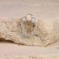 Weißgoldenes Opal-Piercing mit Kettenanhang auf einem beigen Stein