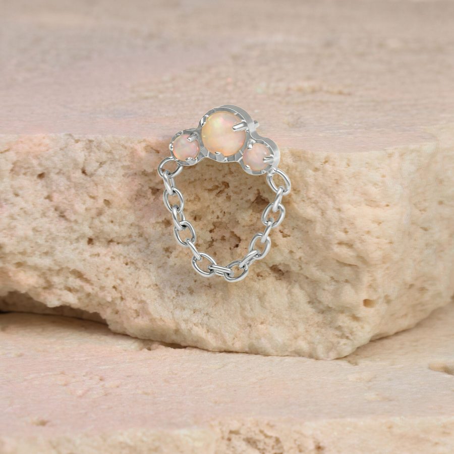 Weißgoldenes Opal-Piercing mit Kettenanhang auf einem beigen Stein