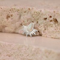 Weißgoldener Piercingaufsatz mit synthetischem Opal in Sonnenstrahlenform auf rosa Stein