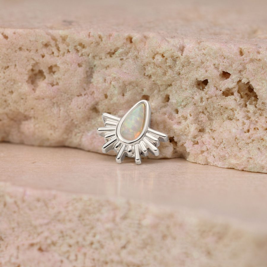 Weißgoldener Piercingaufsatz mit synthetischem Opal in Sonnenstrahlenform auf rosa Stein
