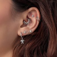 Nahaufnahme eines Ohrs mit mehreren silbernen Piercing-Aufsätzen, darunter ein Turtle-Motiv, auf braunem Haar.