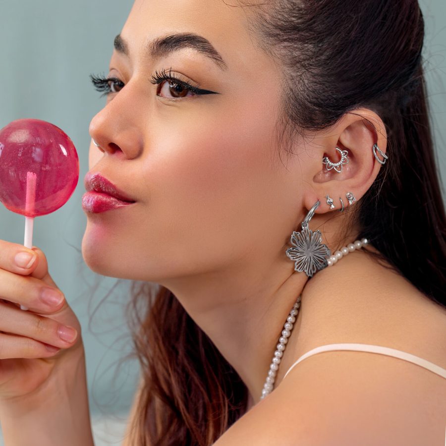 Frau mit mehreren silbernen Ohrpiercings und einem rosa Lollipop, seitlich