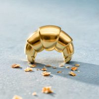 Goldener Croissant-förmiger Aufsatz aus Titan auf hellblauem Hintergrund mit Krümeln