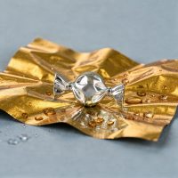 Silberner Bonbon-förmiger Piercingaufsatz auf goldener Folie mit Wassertropfen