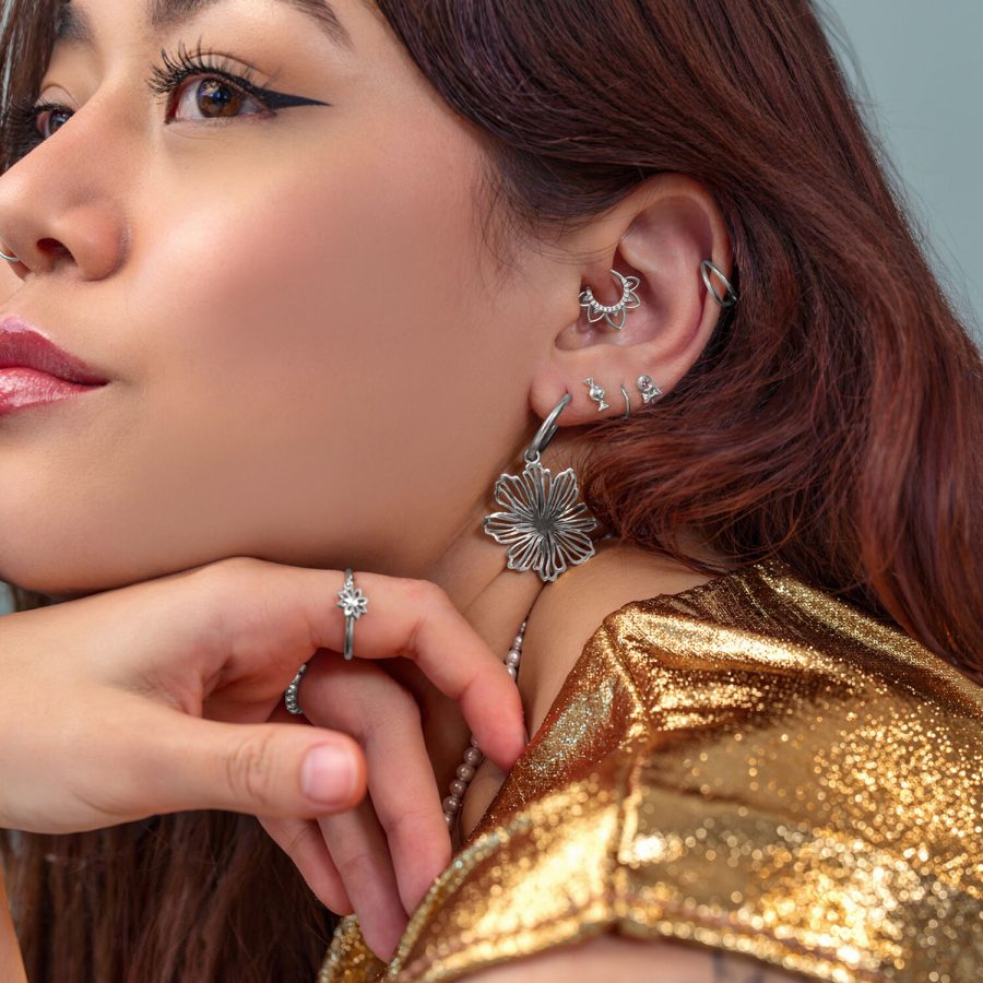 Frau mit mehreren silbernen Ohrringen und Piercings, goldene Kleidung