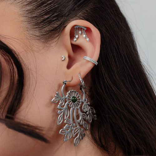 Nahaufnahme eines Ohres mit mehreren silbernen Piercings, darunter ein großer ovaler Anhänger und funkelnde Steckaufsätze.