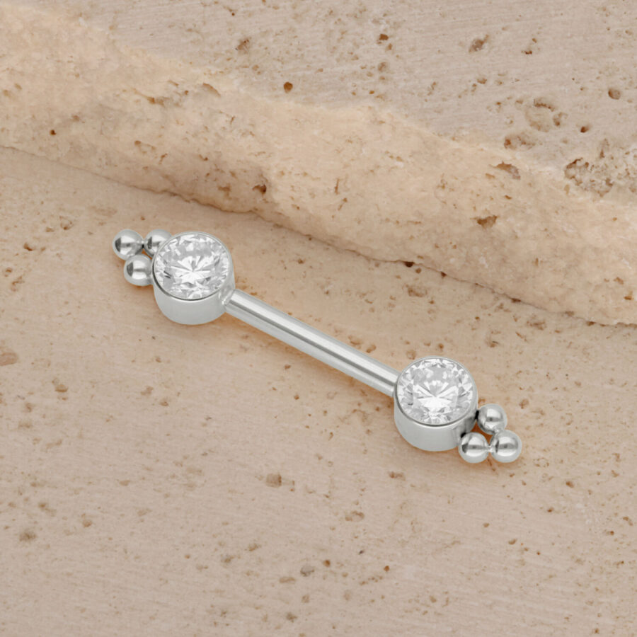 Weißgoldener Titan Barbell mit zwei Zirkonia auf sandigem Hintergrund