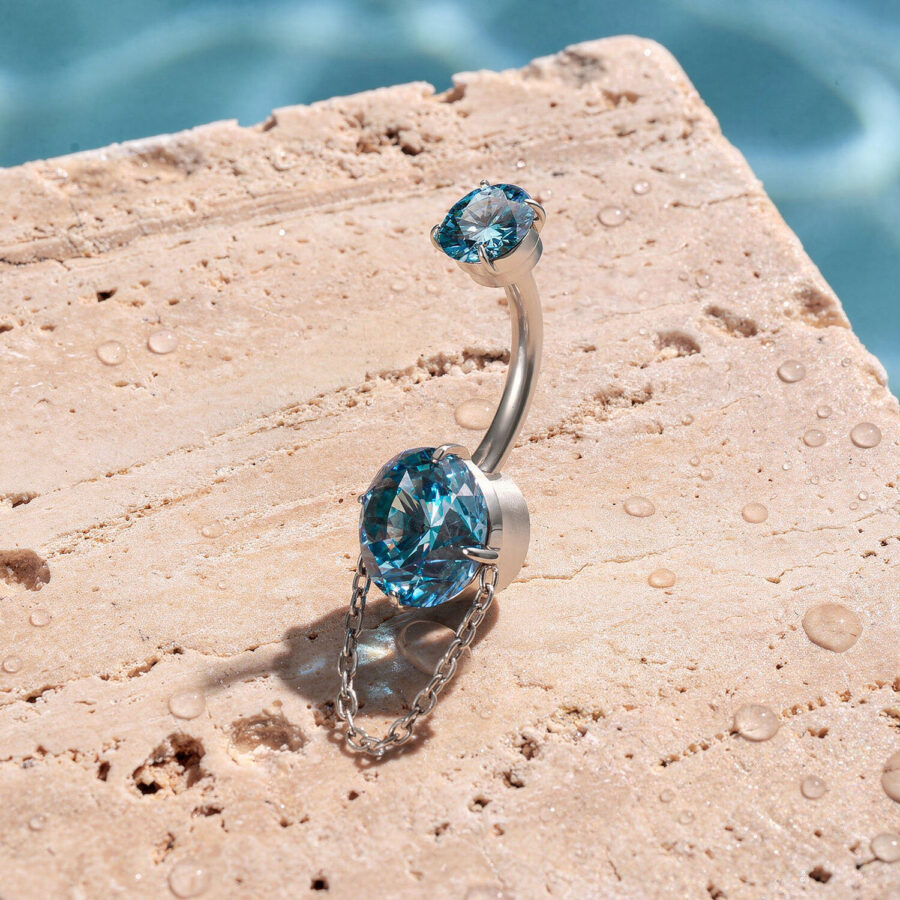 Bauchnabelpiercing mit türkisfarbenen Kristallen und Kette auf Stein