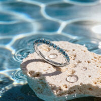 Türkisfarbener Kristallring auf einem hellen Stein am Rand eines Pools mit Sonnenlichtreflexionen