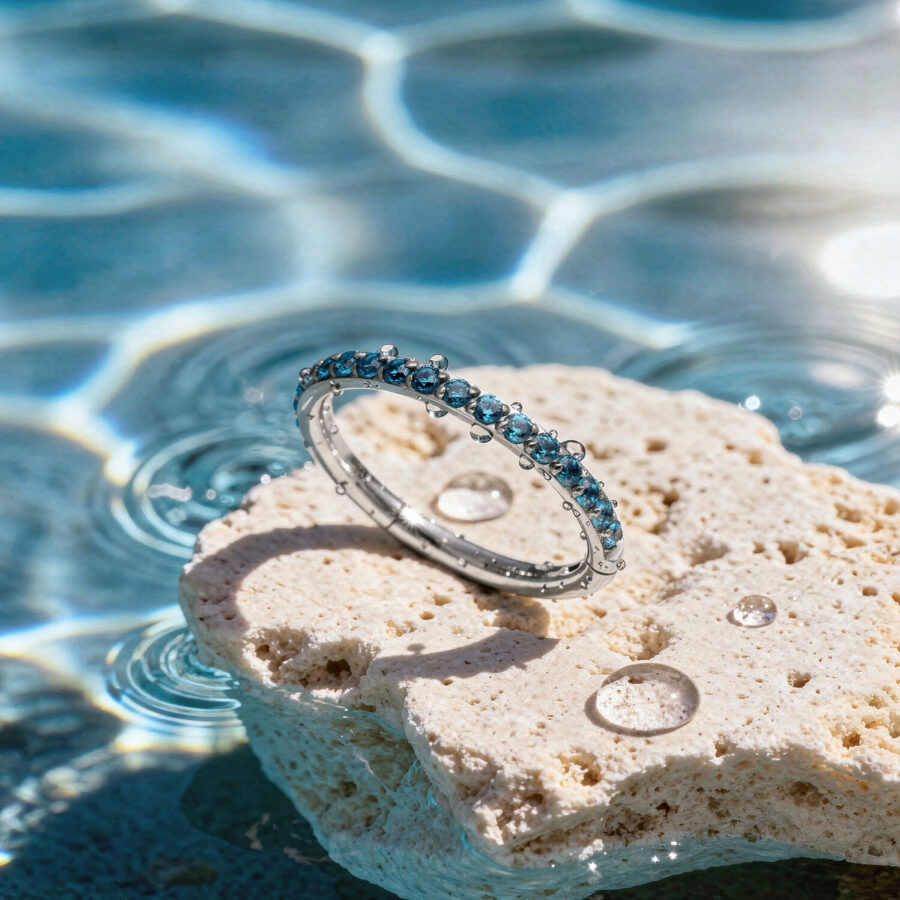 Türkisfarbener Kristallring auf einem hellen Stein am Rand eines Pools mit Sonnenlichtreflexionen
