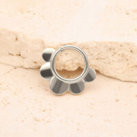 Silberner Half Flower Clicker vor einem beige Stein auf hellem Hintergrund