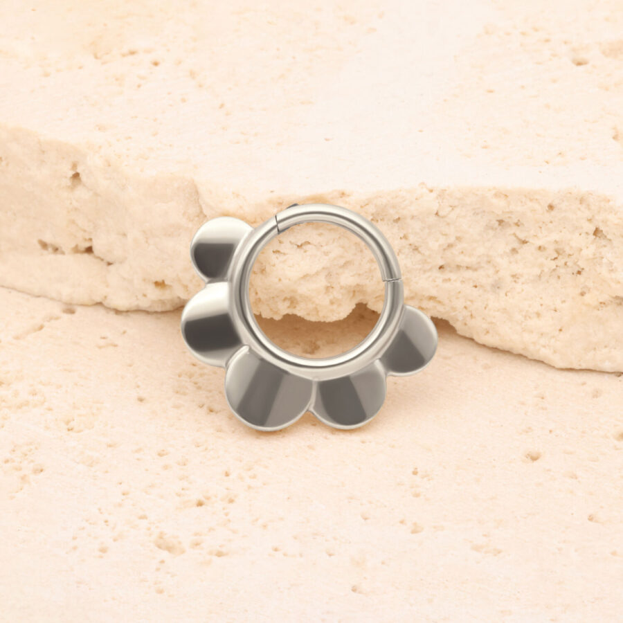 Silberner Half Flower Clicker vor einem beige Stein auf hellem Hintergrund