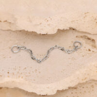 Silberne Piercingkette mit Ringen auf beigem Steinuntergrund